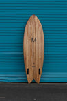  The backside of the wooden fish surfboard also boasts a large M, the logo of Myers Surfboards, who created the shape. Near the bottom of the board, the bizia brand name sits below an albizia project certification logo, signifying the use of albizia wood as regenerative lumber to make this sustainable surfboard. Above the scalloped fish tail are two black futures fin slots.