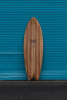 The wooden retro shaped fish surfboard boasts a large M, the logo of Myers Surfboards, who created the shape. Under the M is Bizia's bird logo surrounded by text reading "chambered wood surfboards grown in hawaii".