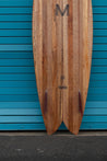 A close-up of the glass-in fins and scalloped fish tail also shows the Myers Surfboards M logo, bizia brand logo and albizia project certification.