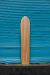 The back of this wooden alaia surfboard does not show the iwa bird engaving found of the front of this ancient surfboard. The board is long and thin, curving softly towards the flat tail.